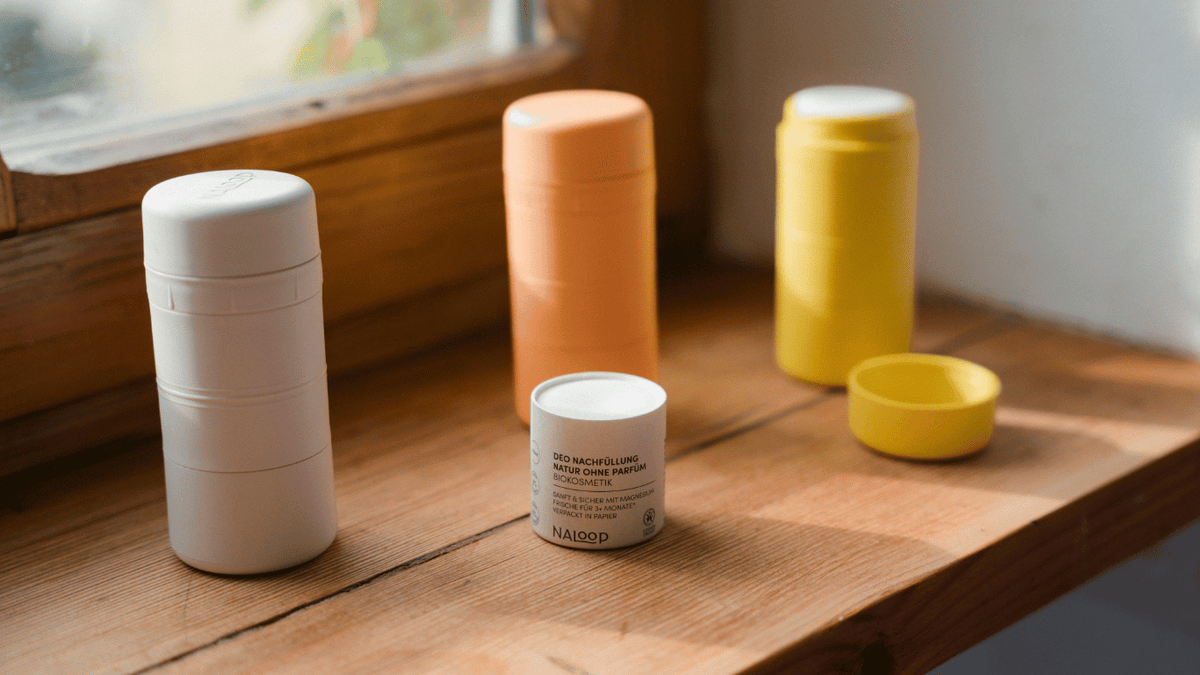Nachfüllbare Naloop Deo-Behälter in Weiß, Orange und Gelb mit Refill auf einem Holztisch