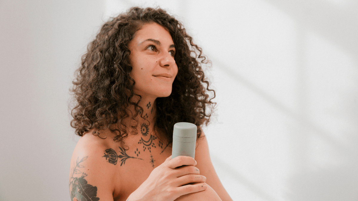 Frau mit Locken und Tattoos hält ein nachfüllbares Naloop Deo in der Hand