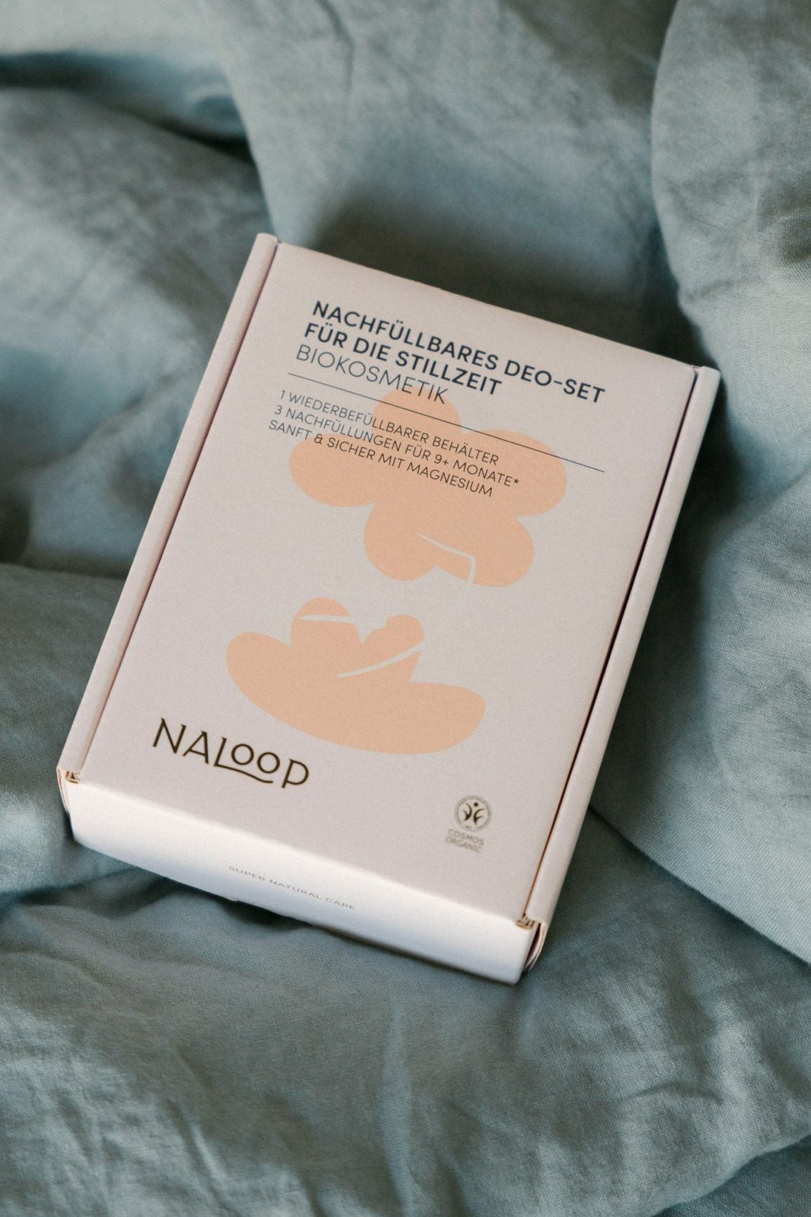 Geschlossene Box des nachfüllbaren Deo-Sets für die Stillzeit von Naloop, Biokosmetik mit Magnesium, auf hellblauer Bettwäsche